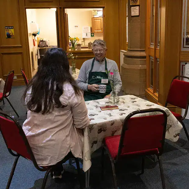 A volunteer at Longridge Food Bank helping a woman at a table.