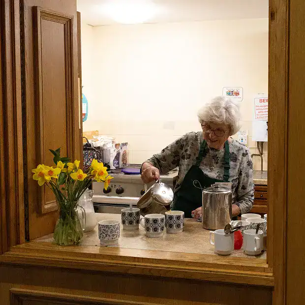 A volunteer woman pouring tea into cups at Longridge Food Bank kitchen.