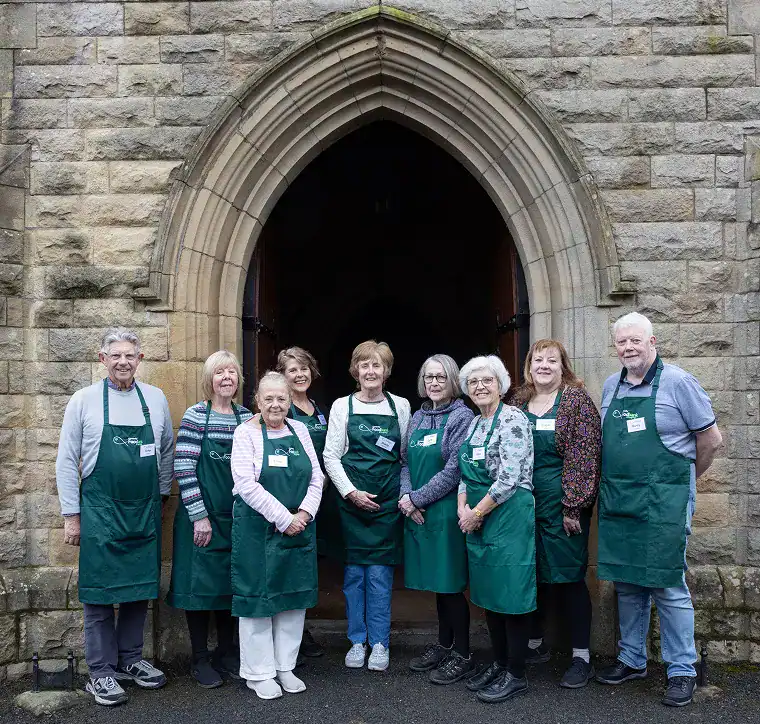 Group of volunteers wearing green aprons standing in front of a church doorway.